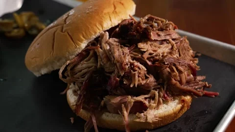 Mouthwatering pulled pork BBQ sandwich on a bun, served on a tray with pickles Stock Footage 346249359