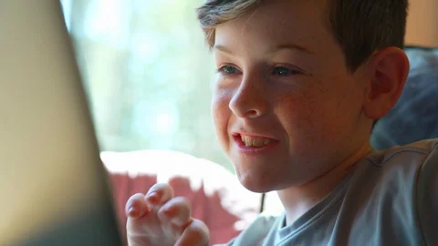 Move from of child’s face  to hands doing schoolwork at home on laptop Stock Footage 129640675