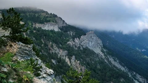 The movement of clouds over a mountain peak covered with pine trees and rocks Stock Footage 140287246