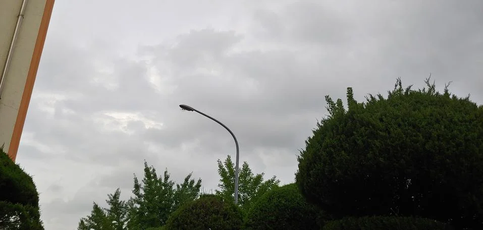 The movement of sky and clouds between the silhouettes of tree and street lam Stock Photos