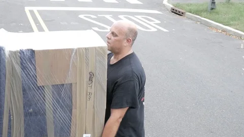 Mover Workers Carrying Wrapped Piece Of Furniture Truck Daytime Handheld Shot Video stock 129499602