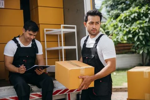 Mover workers in uniform unload boxes checking shipment with a clipboard at the Stock Photos