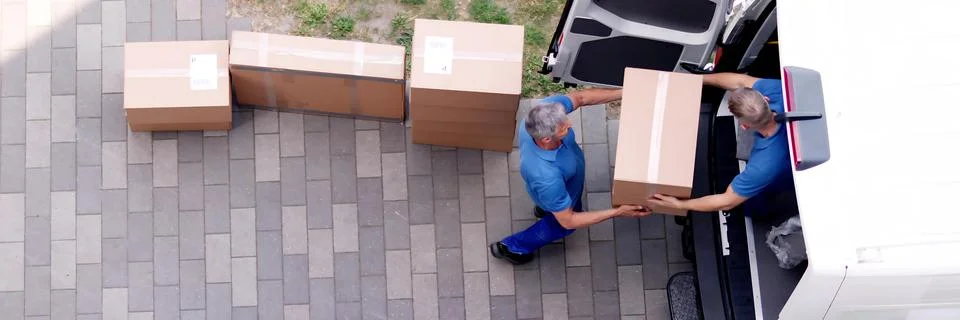 Movers carrying heavy boxes while moving Stock Photos
