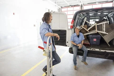 Movers laughing at back of moving van in storage facility loading dock Stockfoto's