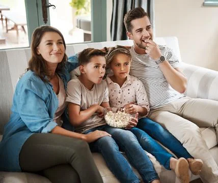 Movies that the whole family love. a happy young family relaxing on the sofa and Stock Photos