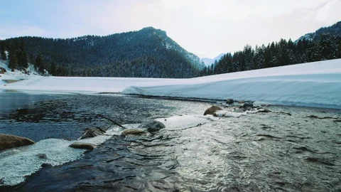 Moving along surface of mountain river as it feeds into snow-covered reservoir Video stock 129421692