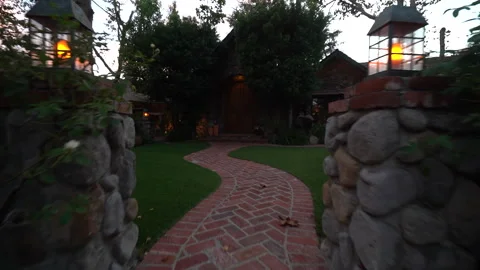 Moving along a winding brick walkway to a stone house at twilight Stock Footage 345529353