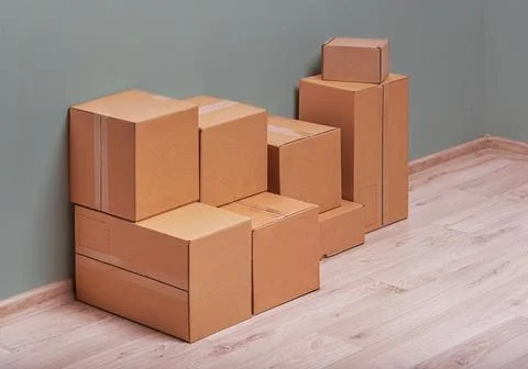 Moving boxes are stacked in the corner of a room with a light wood floor and a Stockfoto's
