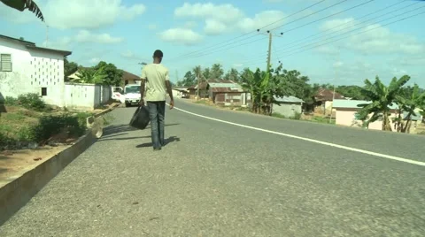 MOVING CAMERA: PAKRO YOUNG MAN CARRIES EMPTY CONTAINER DOWN STREET Stock Footage 58930447