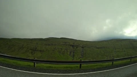 Moving car window view of green hills and road guardrail under overcast sky Stock Footage 339096809
