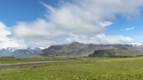Moving clouds over a road running through a green mountain valley on a sunny day Video stock 136978428