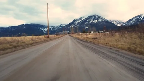 Moving down an empty dirt road with fencing on side and snow capped mountains Stock Footage 125050618