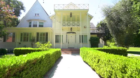 Moving down a hedge lined path toward a white two story house Stock Footage 345680558