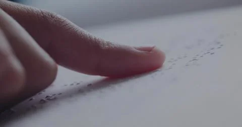 Moving fingertip gently reading raised dot patterns on softly lit desk, with Stockfoto's