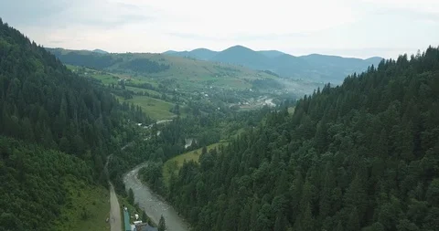 Moving forward above a river and forest to the mountain valley with a village. Video stock 127050099