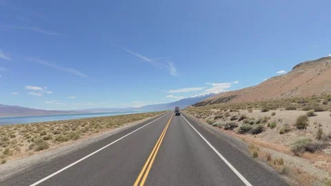 Moving forward on two-lane road between arid desert and bright blue lake Vídeos de archivo 334625485
