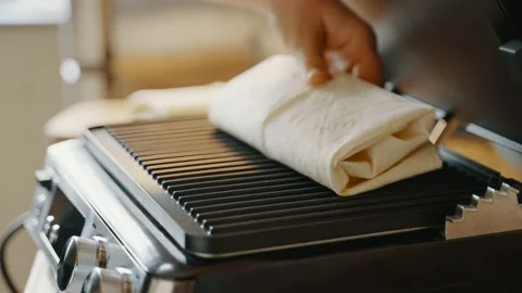Moving lavash with stuffing on an electric grill by a hand for further cooking Stock Footage 234772442