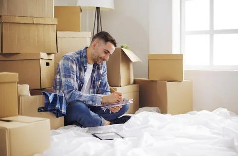 A moving man sitting on the floor in empty apartment, Among the Boxes, Checking Stock Photos