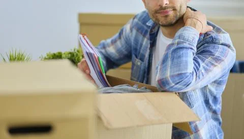 A moving man sitting on the floor in empty apartment, Among the Boxes, Checking Stock-Fotos