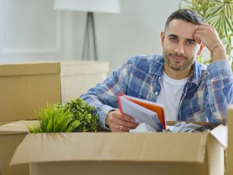 A moving man sitting on the floor in empty apartment, Among the Boxes, Checking Stock Photos