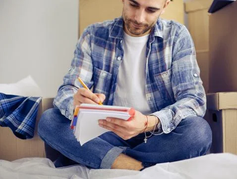 A moving man sitting on the floor in empty apartment, Among the Boxes, Checking Stock Photos