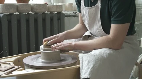On moving potter's wheel master in apron makes dishes with his hands. Stock Footage 88483583