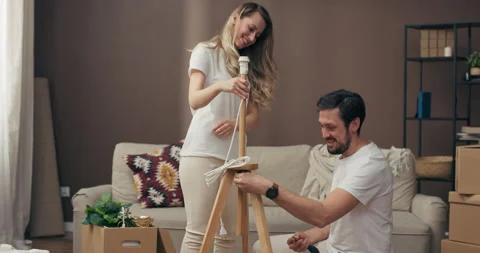 Moving in process delighted husband helping adorable young wife assembling new Vídeos de archivo 219647539