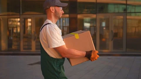 A Moving service employees in uniform walks with a box in his hands background Stock Footage 238979853