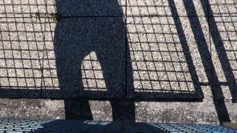 A moving shadow of a man on a stone floor behind a fence Stock Footage 172384123