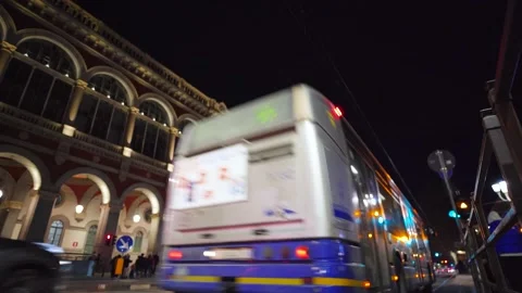 Moving shot of bus passing in front of a big building at night Stock Footage 235398866