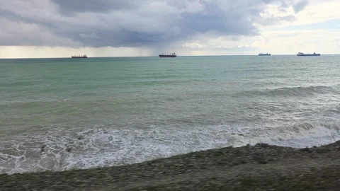 Moving shot from a train window viewing the turbulent sea with several cargo Vidéo 335266529
