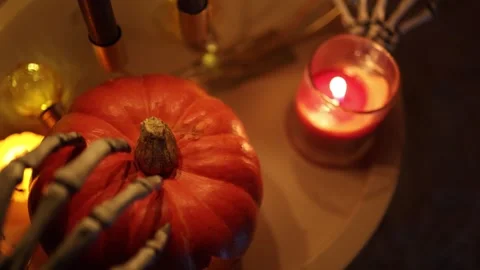 Moving skeleton hand gently strokes pumpkin beside a glowing Halloween candle Stock-Footage 346147425
