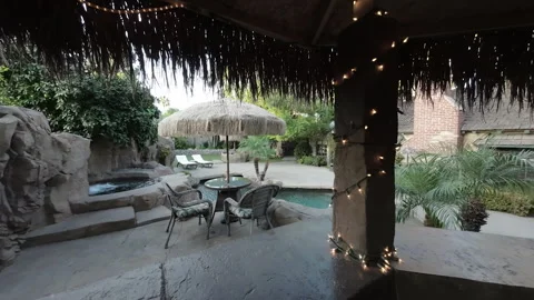 Moving from a thatched outdoor bar to a backyard pool and cottage Stock Footage 345542758
