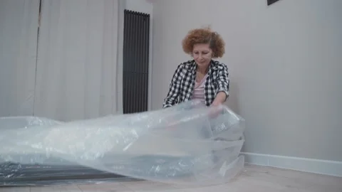 Moving theme. Elderly female in good mood is unwrapping new orthopedic mattress Stock Footage 165628675