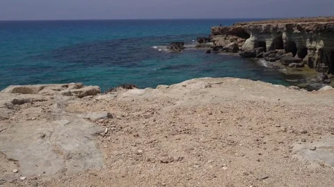 Moving towards the cliff edge and looking down to stones in blue surf. POV Stock Footage 76988349