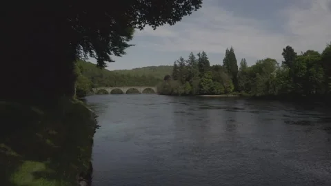 Moving towards Dunkeld Bridge under trees crowns along river surface with green Vídeos de archivo 251047047