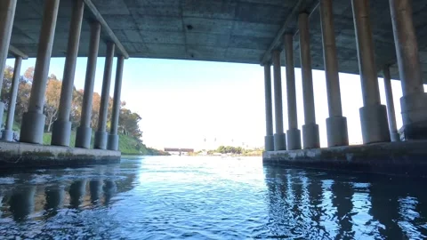 Moving under concrete bridge pillars into sunny Carlsbad Lagoon water. Stock Footage 331765684