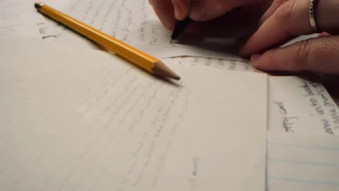Moving wide macro shot across a tabletop of papers as writer jots some notes 8K Vídeo Stock 122561041