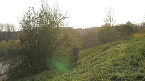 Mowing trimmer. Worker cutting grass in green yard at sunset Stock Footage 106922712