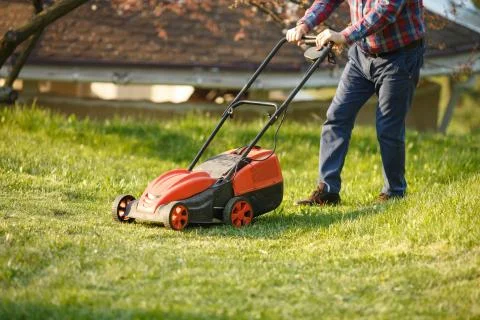 Mowing trimmer - worker cutting grass in green yard at sunset. Man with electric Stock Photos