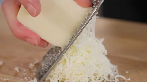 Mozzarella cheese is grated using a fine grater on a wooden table. Close-up Stock Footage 262621712