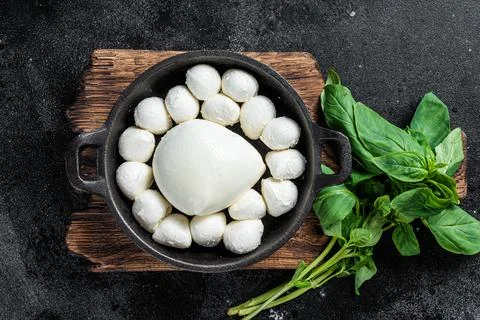 Mozzarella cheese mini balls in pan with basil. Black background. Top view Stock Photos