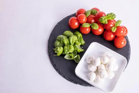 Mozzarella in a cup, basil and tomatoes on a stone tile Stock Photos