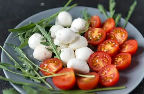 Mozzarella  with cut in half cherry tomatoes and arugula on a plate on a dark Stock Photos