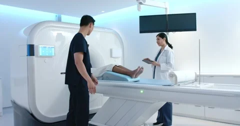 MRI team checking African patient position, tech fixing pad, sliding into bore, Stock Footage 343099178