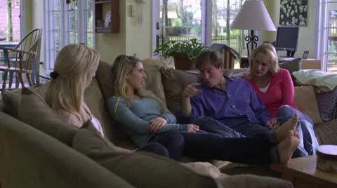 MS, DS, family sitting on a couch in living room listening to Dad tell a funny Stock Footage