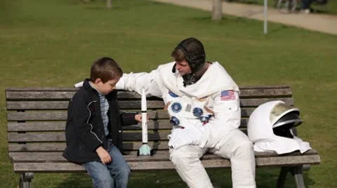 MS, Lockdown of an astronaut and a young boy sitting on a park bench playing Stock Footage 10700675