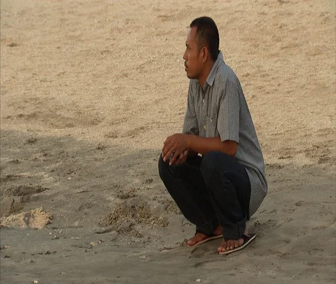 MS Man squatting in thought in wet sand at beach Stock Footage 86747220