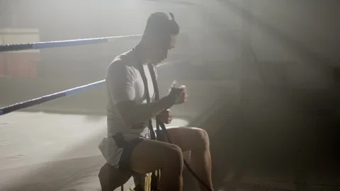 Muay Thai fighter puts on hand wraps while sitting on the edge of a boxing ring 스톡 동영상 104553264