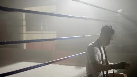 Muay Thai fighter wraps hands while sitting on the edge of a boxing ring 스톡 동영상 104553928
